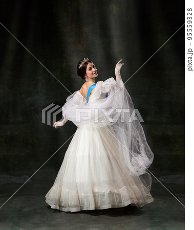 Young queen. Portrait of adorable girl in image of medieval royal person in renaissance style dress isolated on dark background. Comparison of eras, beauty, history, art 95559328
