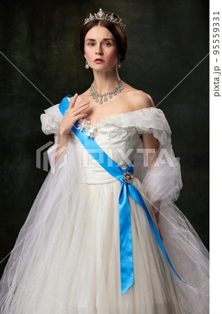 Young queen. Portrait of adorable girl in image of medieval royal person in renaissance style dress isolated on dark background. Comparison of eras, beauty, history, art Young queen. Portrait of adorable girl in image of medieval royal person in renaissance style dress isolated on dark background. Comparison of eras, beauty, history, art 95559331