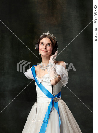 The favorite music. Elegant woman, royal person, queen or princess in white medieval outfit listening to music on dark vintage background. 95559338