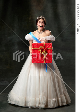 Christmas present. Young queen. Portrait of adorable girl in image of medieval royal person in renaissance style dress isolated on dark background. Comparison of eras, beauty, history, art 95559384