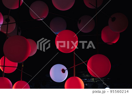 red and white modern pendant lamps, plastic spherical chandeliers. Illuminated lamp hanging against black background. 95560214