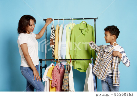 Portrait of woman, mother doing clothes shopping with teen boy, son over blue background. Trying on shirt Portrait of woman, mother doing clothes shopping with teen boy, son over blue background. Trying on shirt 95560262