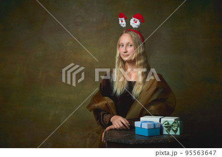 Silly mood. Beautiful young girl with long blonde hair wearing medieval dress over dark vintage background. Retro style, art, fashion, comparison of eras concept. Silly mood. Beautiful young girl with long blonde hair wearing medieval dress over dark vintage background. Retro style, art, fashion, comparison of eras concept. 95563647