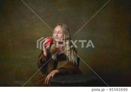 Beautiful young girl with long blonde hair wearing medieval dress posing over dark vintage background. Retro style, art, fashion, comparison of eras concept. 95563690