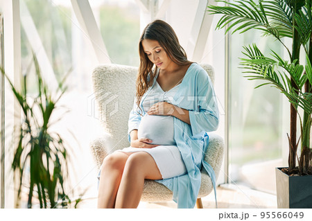Pregnant happy woman touching her belly rest on chair at modern home Pregnant happy woman touching her belly rest on chair at modern home 95566049