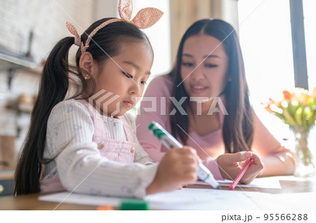 Woman observing her kid doodling on the sheet of paper Woman observing her kid doodling on the sheet of paper 95566288