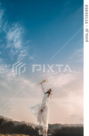 青空のもとで花を掲げる白いワンピースの女性 青空のもとで花を掲げる白いワンピースの女性 95566868