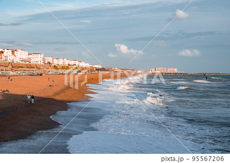 People walking down the promenade near the beach in Brighton. Holiday town by the sea. Enjoying Brighton vibe in England. 95567206