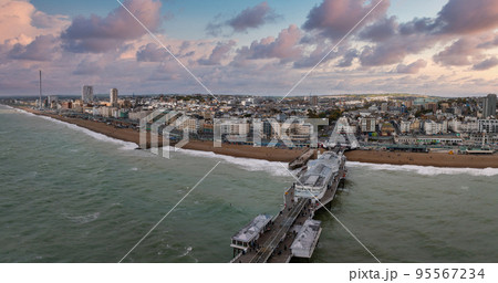 Aerial view of Brighton Palace Pier, with the seafront behind. Aerial shot of the stunning city of Brighton and Hove with seagulls flying around at sunset. 95567234