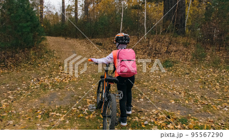 One caucasian children walk with bike in autumn park. Little girl walking black orange cycle in forest. Kid goes do bicycle sports. Biker motion ride with backpack and helmet. Mountain bike hard tail. One caucasian children walk with bike in autumn park. Little girl walking black orange cycle in forest. Kid goes do bicycle sports. Biker motion ride with backpack and helmet. Mountain bike hard tail. 95567290