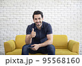 Lifestyle portrait of attractive handsome man with pleasant smile relaxing and sitting on yellow sofa at living room 95568160