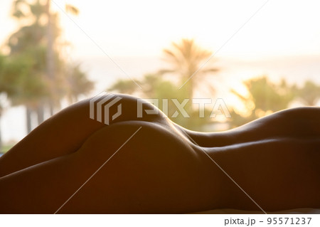 Silhouette of naked woman with beautiful buttocks lying on the sunbed against sea and palm trees at summer sunny sunset day 95571237