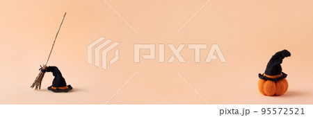 Halloween concept. A black hat and a witch's broom and knitted orange pumpkin with a black witch hat on an orange background, front view, copy space 95572521