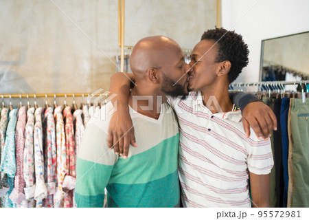 Happy young African gay couple kissing in modern boutique 95572981