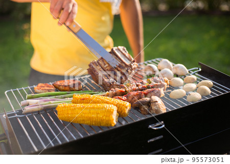 Close-up of man grilling tasty meat and vegetables on sunny day 95573051