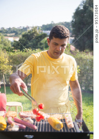 Pleased mid adult man grilling steak and corn 95573084
