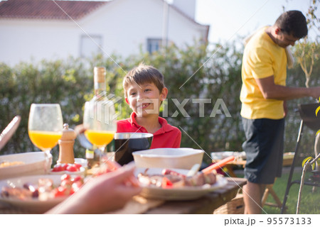 Smiling little boy eating BBQ at backyard Smiling little boy eating BBQ at backyard 95573133