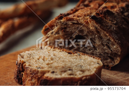 dark yeast-free buckwheat bread in a cut lies on a cutting wooden board on a wooden table next to italian grissini on a linen tablecloth in rustic style. Selective focus. Concept of making breakfast. dark yeast-free buckwheat bread in a cut lies on a cutting wooden board on a wooden table next to italian grissini on a linen tablecloth in rustic style. Selective focus. Concept of making breakfast. 95573704