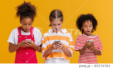 Funny delighted multinational kids use smartphone on yellow background 95574763