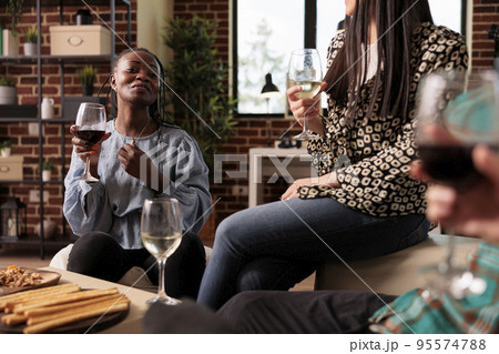 African american young adult woman laughing, smiling, guffawing, having fun at various ethnicities, nationalities friends social reunion, gathering, drinking wine, eating appetizers. African american young adult woman laughing, smiling, guffawing, having fun at various ethnicities, nationalities friends social reunion, gathering, drinking wine, eating appetizers. 95574788
