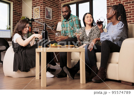 Different ethnicities couples drinking wine, alcohol, sitting at apartment living room.Culturally diverse mates chatting, talking, conversing, enjoying social life at gathering. Different ethnicities couples drinking wine, alcohol, sitting at apartment living room.Culturally diverse mates chatting, talking, conversing, enjoying social life at gathering. 95574789