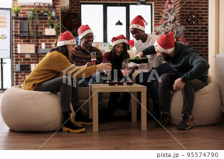 Colleagues drinking bottle of wine at xmas party event in festive office with christmas tree and decorations. Coworkers celebrating winter holiday festivity at work with ornaments and alcohol. Colleagues drinking bottle of wine at xmas party event in festive office with christmas tree and decorations. Coworkers celebrating winter holiday festivity at work with ornaments and alcohol. 95574790