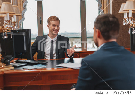Smiling hotel receptionist helping Businessman to check in and receive key from room Smiling hotel receptionist helping Businessman to check in and receive key from room 95575392