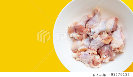 Fresh raw chicken wings (wingstick) in white bowl on yellow background. Fresh raw chicken wings (wingstick) in white bowl on yellow background. 95576152