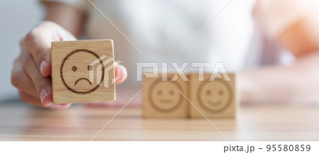 Hand choosing unhappy angry face from Emotion block. customer review, bad experience, negative feedback, satisfaction, survey, rating service, assessment, mood, world mental health day concept 95580859