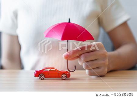 Businesswoman hand holding red umbrella and cover red car toy on table. Car insurance, warranty, repair, Financial, banking and money concept 95580909