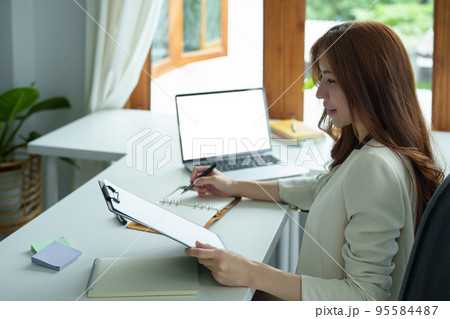 Portrait of an Asian bank employee using notebooks to take notes, budget documents and computers to close financial statements. 95584487
