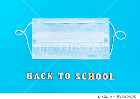 Back to school. The inscription in wooden letters and a protective medical mask on a blue background Back to school. The inscription in wooden letters and a protective medical mask on a blue background 95585650