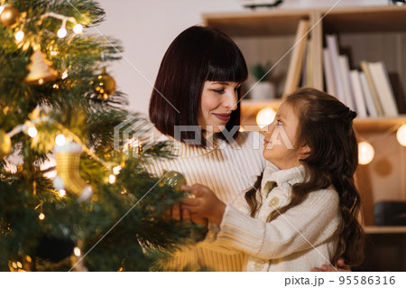 Happy mother and little daughter decorating christmas tree at home. Happy mother and little daughter decorating christmas tree at home. 95586316