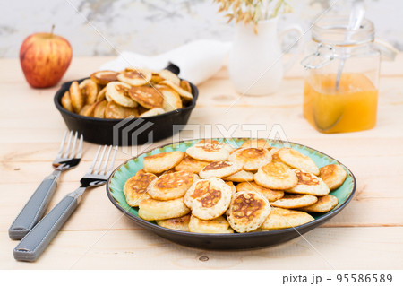 Trend breakfast. Dutch mini pancakes on a plate and a frying pan with them on a wooden table. 95586589