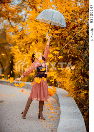 Beautiful girl in a dress with an umbrella in the autumn park. She holds him over her head, autumn leaves are falling out of him Beautiful girl in a dress with an umbrella in the autumn park. She holds him over her head, autumn leaves are falling out of him 95589147
