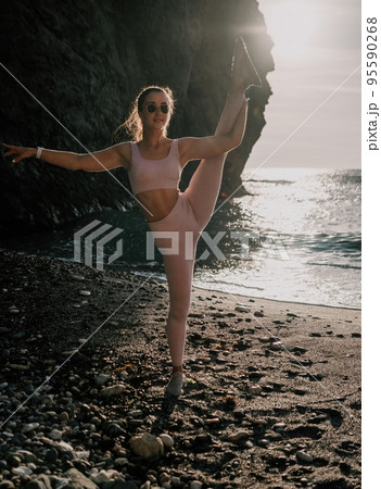 Young woman with black hair, fitness instructor in pink leggings and tops doing stretching and pilates on volcanic rocks near the sea on sunset. Female fitness yoga routine concept. Healthy lifestyle. Young woman with black hair, fitness instructor in pink leggings and tops doing stretching and pilates on volcanic rocks near the sea on sunset. Female fitness yoga routine concept. Healthy lifestyle. 95590268