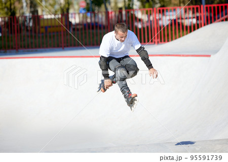Mature male inline roller training in public skate park. Practicing jumps, tricks. Concept of active lifestyle, sport, hobbies. 95591739