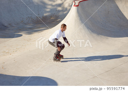 Mature male inline roller training in public skate park. Practicing jumps, tricks. Concept of active lifestyle, sport, hobbies. 95591774