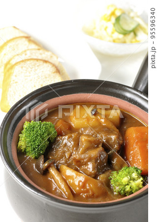 お鍋にブロッコリーや人参、しめじなど沢山の具材が入っているビーフシチューとサラダとパン 95596340
