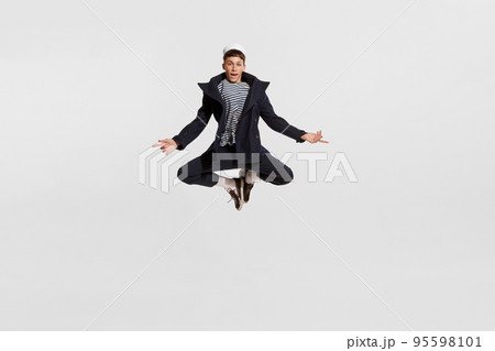 Portrait of young boy, sailor in striped shirt and jacket posing in a jump isolated over white background 95598101