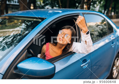A young angry woman peeks out of the car window 95600648