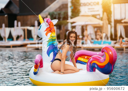 Woman on inflatable unicorn toy mattress float in pool. 95600672