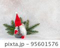 Christmas gnome in red hat side view with fir branch holiday card on light winter background 95601576