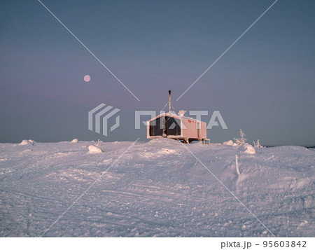 Cozy cottage on a snowy mountain slope. There is a full red moon in the dark sky. Harsh northern nature. Cozy cottage on a snowy mountain slope. There is a full red moon in the dark sky. Harsh northern nature. 95603842