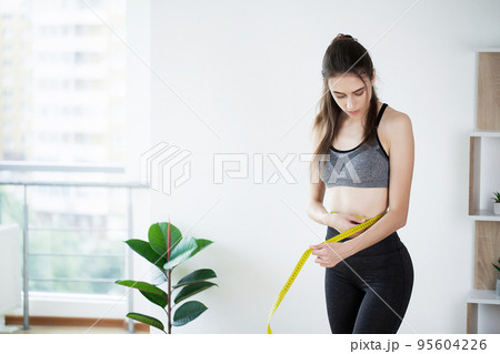 Slim young woman measuring her thin waist with a tape measure 95604226
