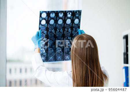 Young female doctor looking attentively at x-ray Young female doctor looking attentively at x-ray 95604487