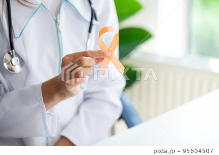Doctor holding and showing orange awareness ribbon in her hands Doctor holding and showing orange awareness ribbon in her hands 95604507