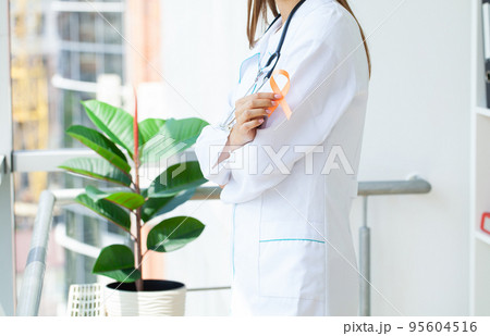 Doctor holding and showing orange awareness ribbon in her hands 95604516