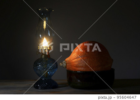 orange Hokkaido pumpkin in a ceramic bowl and a burning oil lamp 95604647
