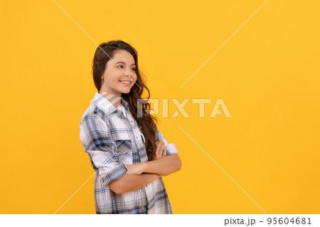 positive teen girl in checkered shirt and with long curly hair on yellow background 95604681